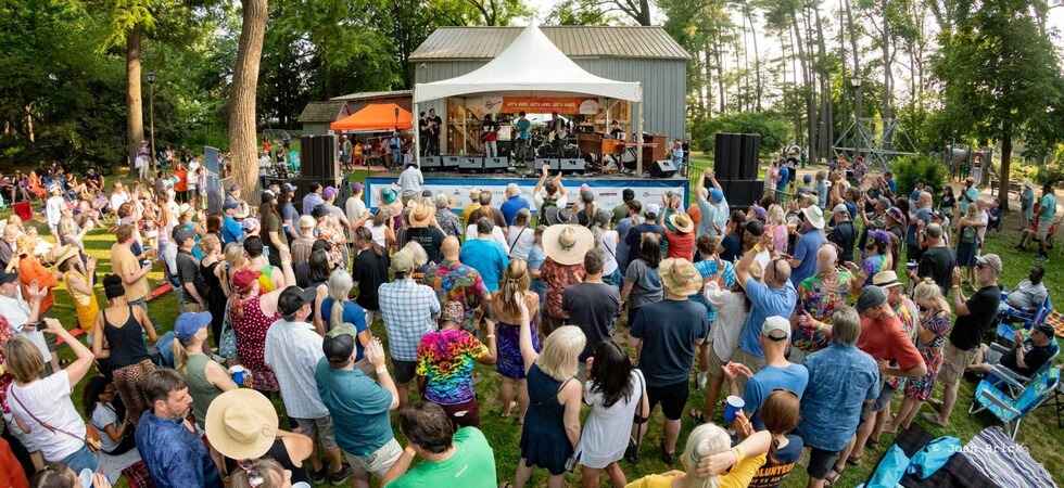Full color photo depicting a crowd enjoying a band playing live music at the Tinner Hill Music Festival in Cherry Hill Park in Falls Church City, Virginia